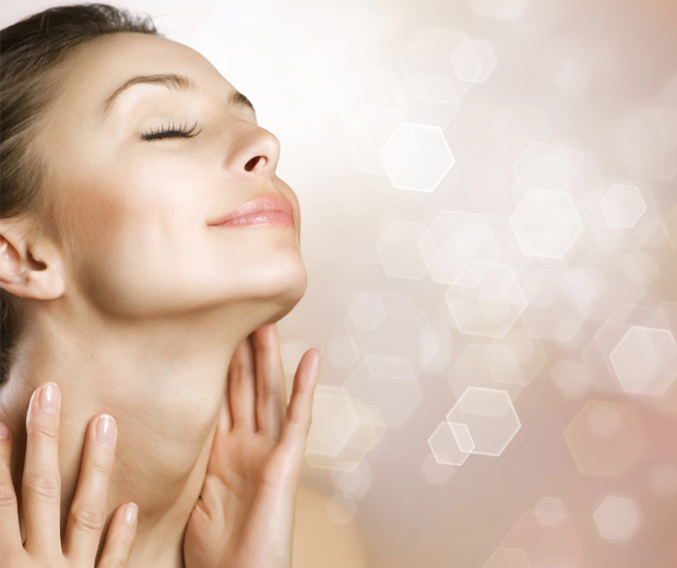 Young woman touching her neck with eyes closed staring upwards on blurry peach color background. Slimwave Electronic Muscle Stimulation technology for your face. Created to reverse aging.