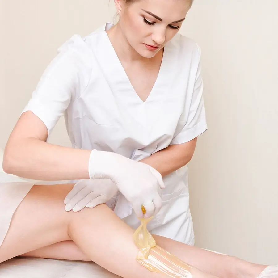 Esthetician waxing female legs in the spa center beauty salon square