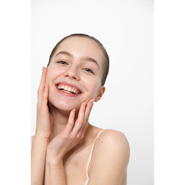 Une femme souriante touche son visage, illustrant un traitement laser non ablatif.